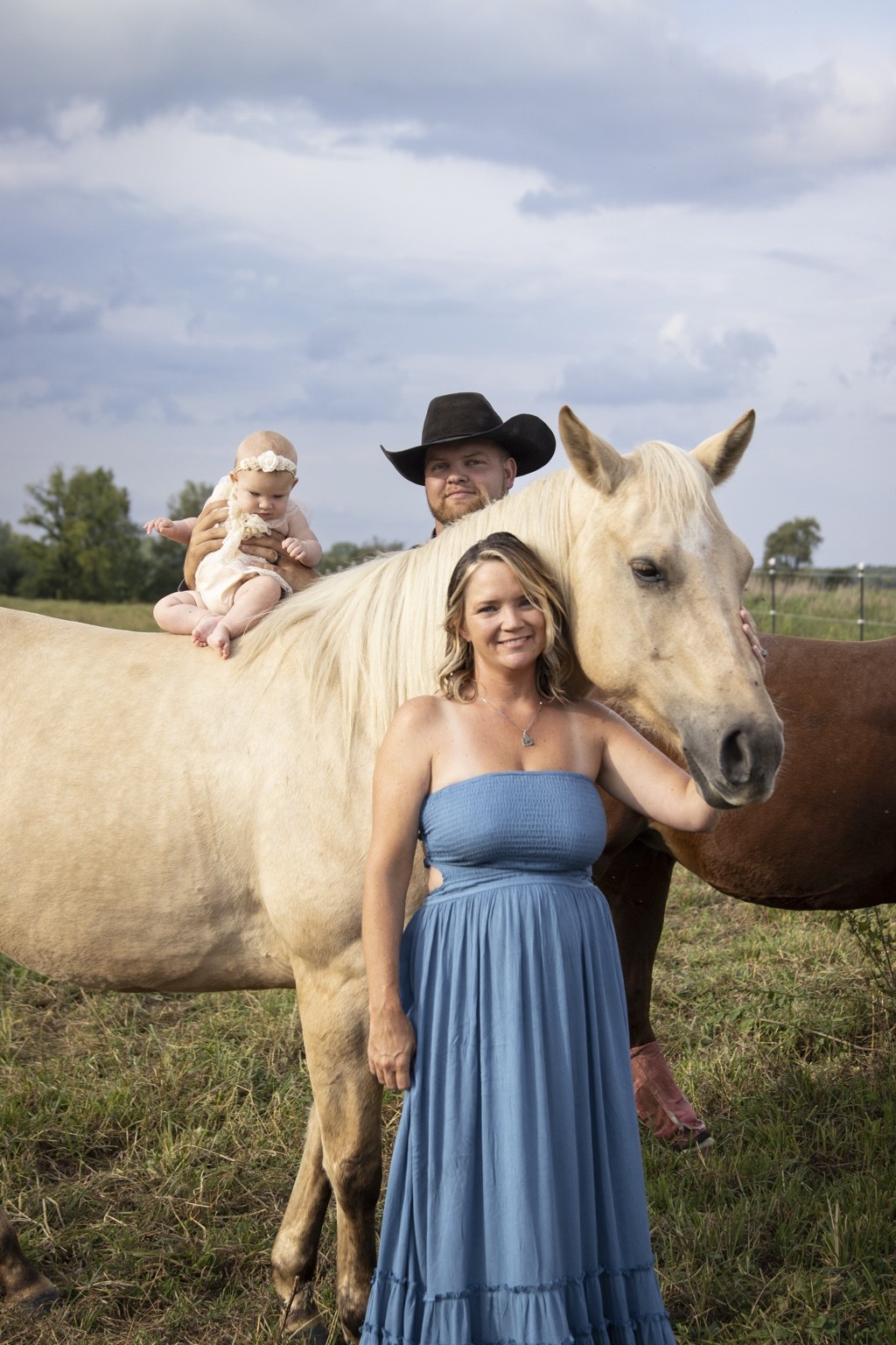 Woman standing beside a light-colored horse with a child on its back