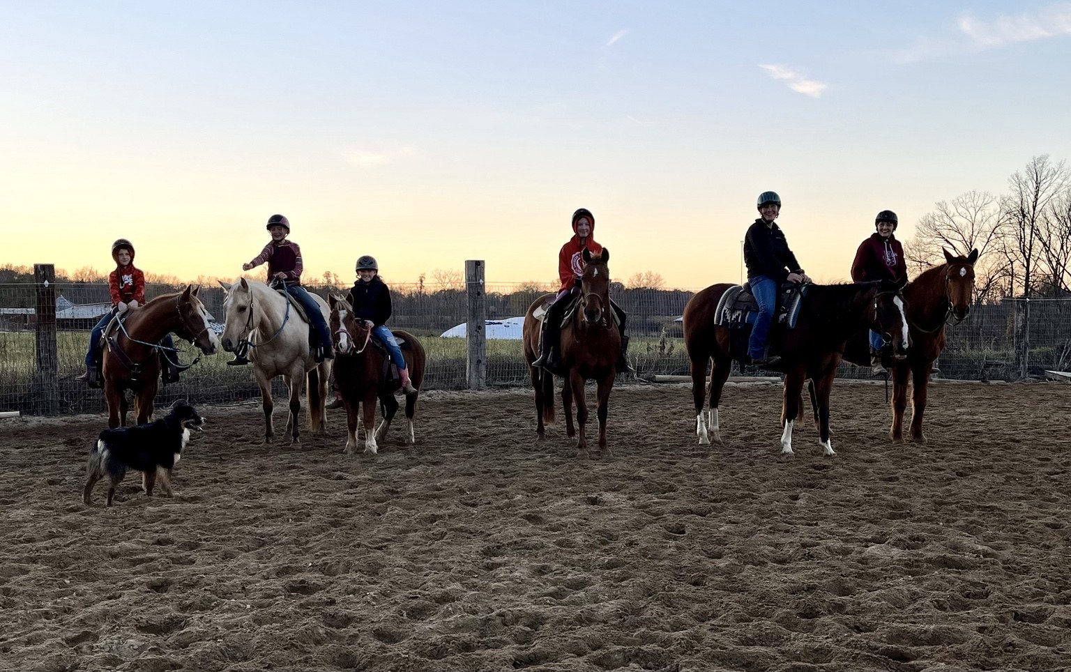Group of riders and horses together in an outdoor arena at sunset