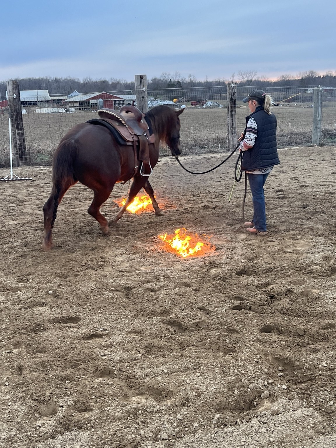 Horse and handler working beside small flames in an outdoor arena
